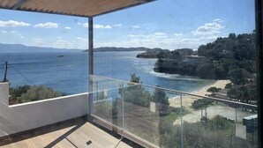A balcony with a glass railing overlooking a coastal landscape, including a beach and distant hills. - Royal Villa 2 (Skiathos)