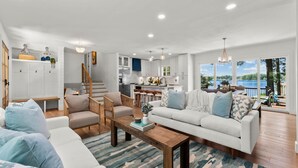 A spacious living room with a large sofa, two armchairs, and a coffee table. A kitchen is visible in the background, and there is a balcony with a view of the lake. - Lakefront Living W/optional Boat Rental (Mooresville)
