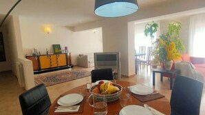 Ein Essbereich mit einem Tisch für vier Personen, einem Fernseher und einer Couch im Hintergrund.