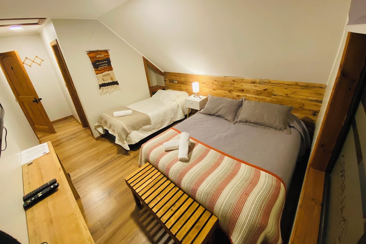 A small, cozy room with a single bed, a wooden bench, and a nightstand with a lamp.