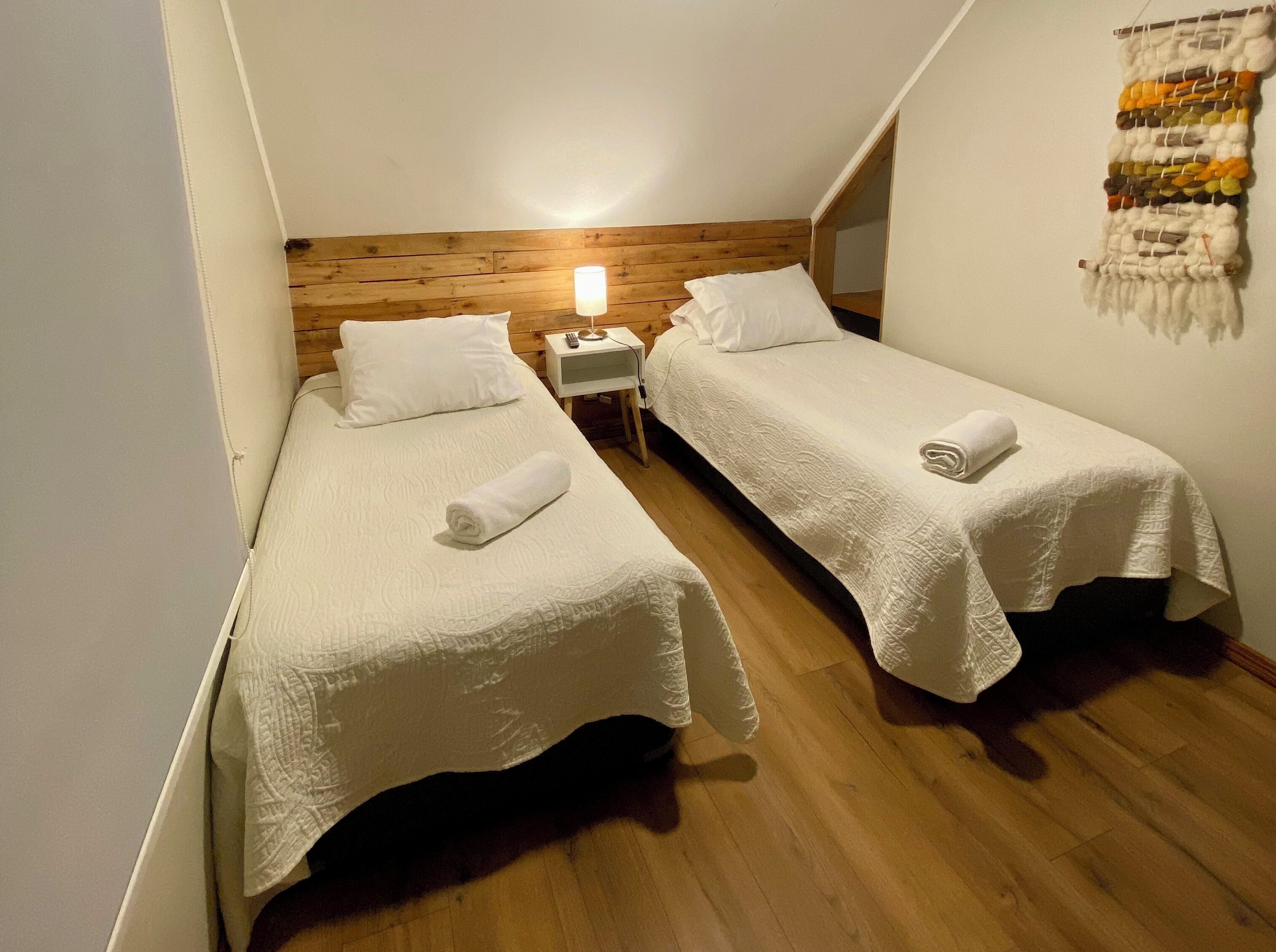 A small, cozy room with two single beds, a nightstand with a lamp, and a wooden headboard.