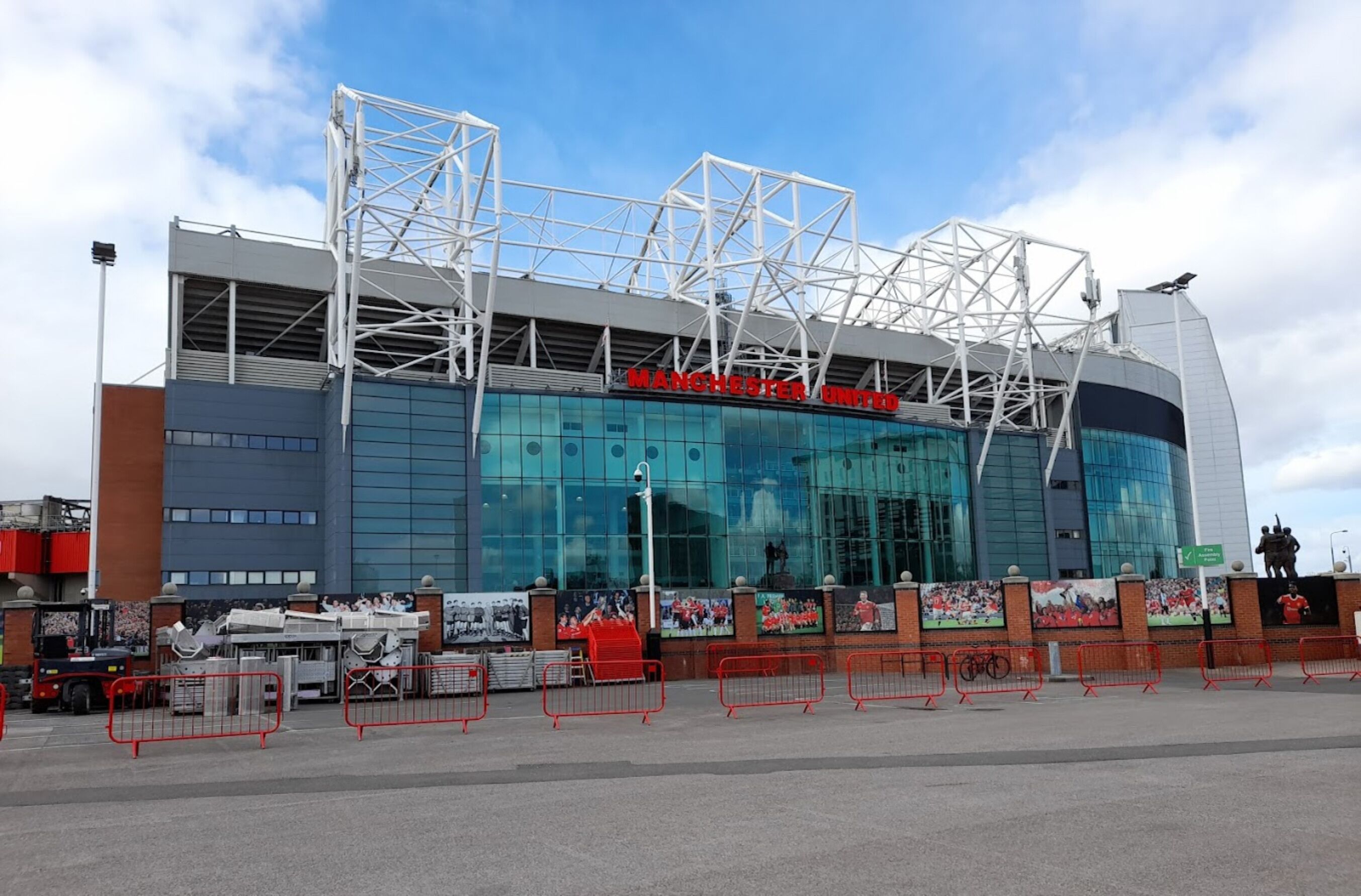 A modern stadium with a prominent "Manchester United" sign, featuring a glass facade and a distinctive white framework.