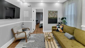 A modern living room with a sofa, a chair, a TV mounted on the wall, and a painting on the wall.