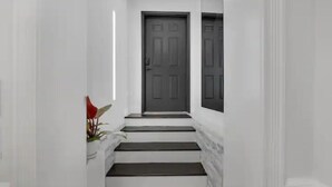 A narrow hallway with white walls and dark steps leading to a dark door.