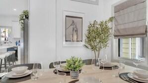 Un comedor con una mesa dispuesta para cuatro personas, una planta en maceta y una obra de arte enmarcada en la pared.