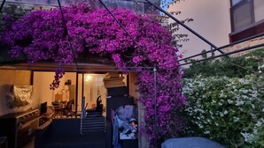 Une entrée extérieure avec un escalier menant à un espace abrité, entouré de bougainvilliers violets et de fleurs blanches.