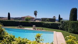 Une piscine à l’eau d’un bleu cristallin, entourée de haies bien entretenues et offrant une vue sur un paysage côtier.