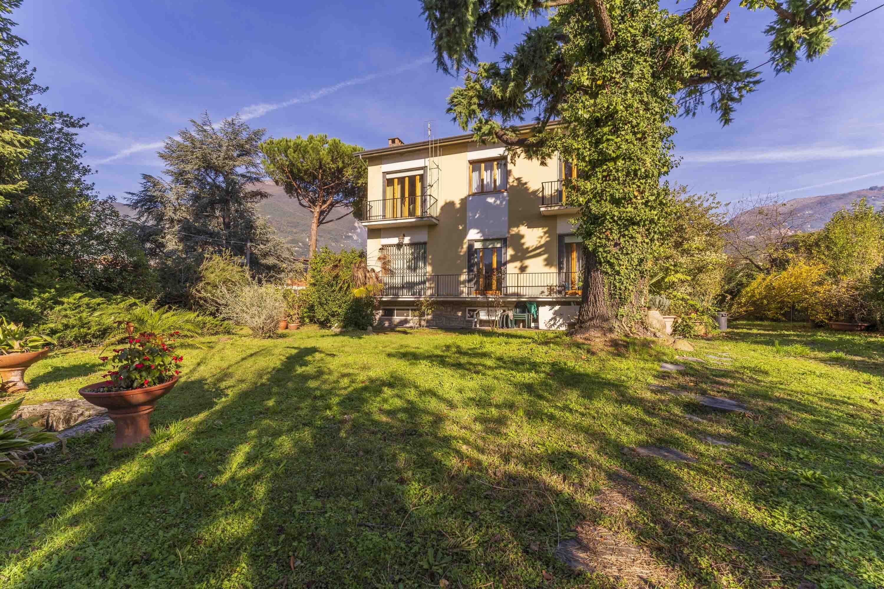A two-story house with a well-maintained lawn, a large tree in the front yard, and a clear view of the surrounding landscape.