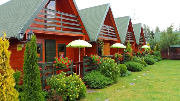 A row of wooden cabins with sloped roofs and green awnings, surrounded by well-maintained gardens and a grassy lawn.