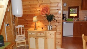 A wooden interior with a dining area, a cabinet with drawers, a table, a chair, a lamp, and a potted plant. - Holiday House in Sarbinowo near Baltic Beach (Sarbinowo)