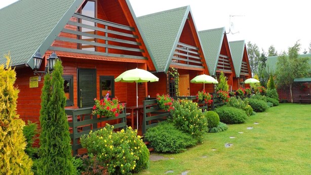 A row of wooden cabins with sloped roofs, each with a porch and outdoor seating. - Holiday House in Sarbinowo near Baltic Beach (Sarbinowo)