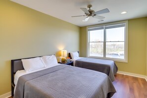 Two beds with grey bedspreads, a ceiling fan, and a window with blinds.