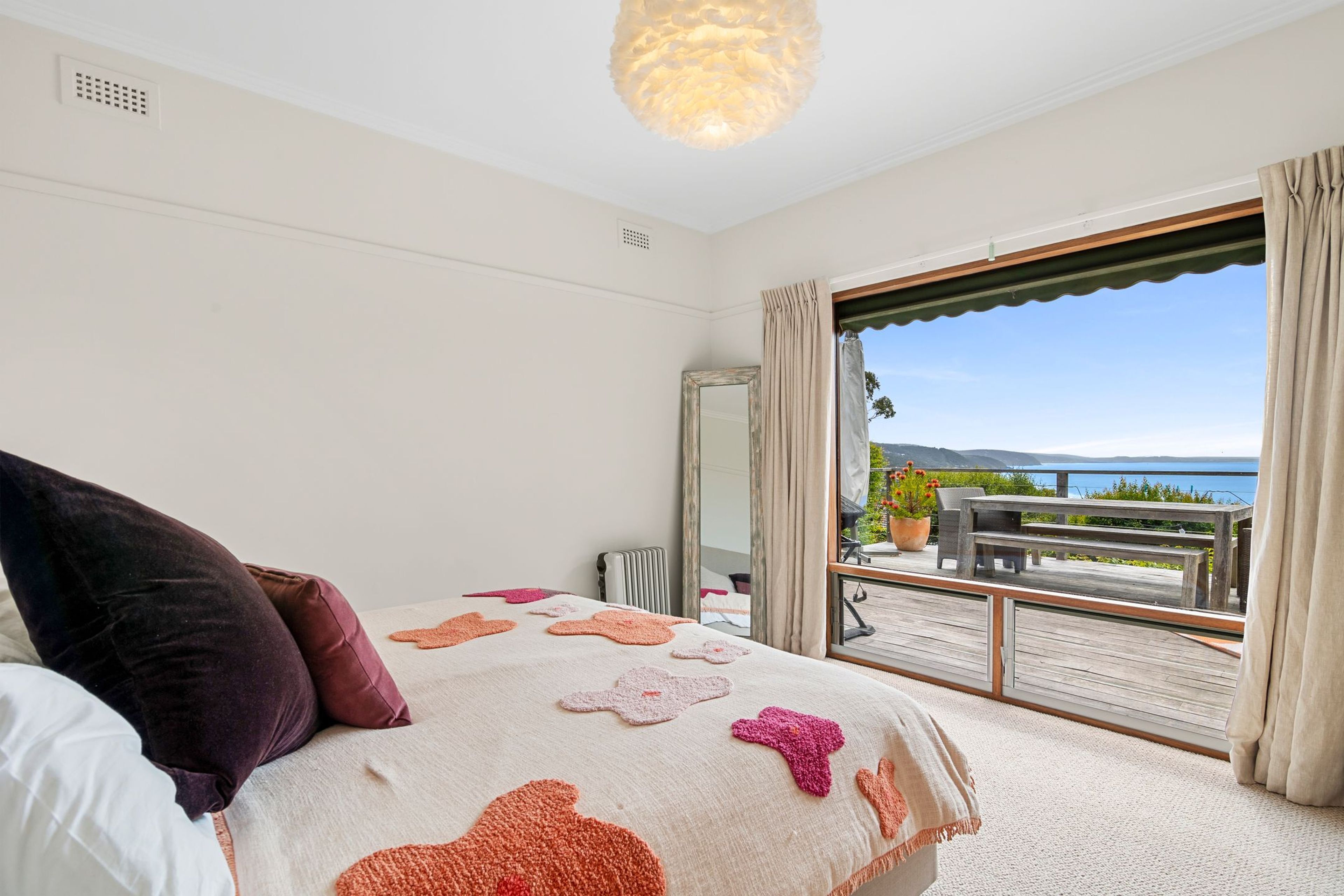 A bedroom with a large bed, a view of the outdoors, and a balcony with outdoor furniture.