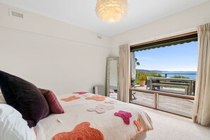 A bedroom with a large bed, a view of the outdoors, and a balcony with outdoor furniture.