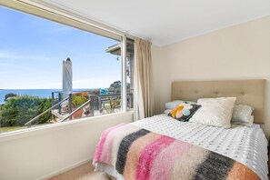 Une chambre dotée d’une grande fenêtre, d’un lit recouvert d’une couvre-lit à motifs et offrant une vue sur un balcon aménagé avec du mobilier d’extérieur.