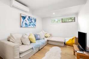 A modern living room with a sectional sofa, a flat-screen TV, and a painting on the wall. - Sunrise - Tranquility of beachfront living (Lorne)