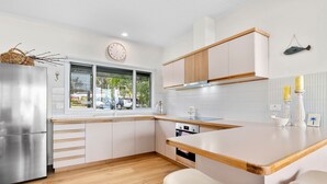 Een moderne keuken met witte kasten, een roestvrijstalen koelkast, houten aanrechtbladen en een raam met uitzicht.