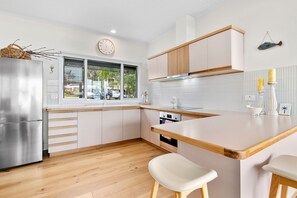 A modern kitchen with white cabinetry, a stainless steel refrigerator, wooden countertops, and a window with a view of the outside. - Sunrise - Tranquility of beachfront living (Lorne)