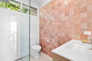 A modern bathroom with a glass shower enclosure, a white toilet, and a white sink with a wooden countertop.