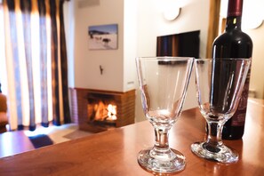 Two empty wine glasses on a wooden table with a fireplace in the background.