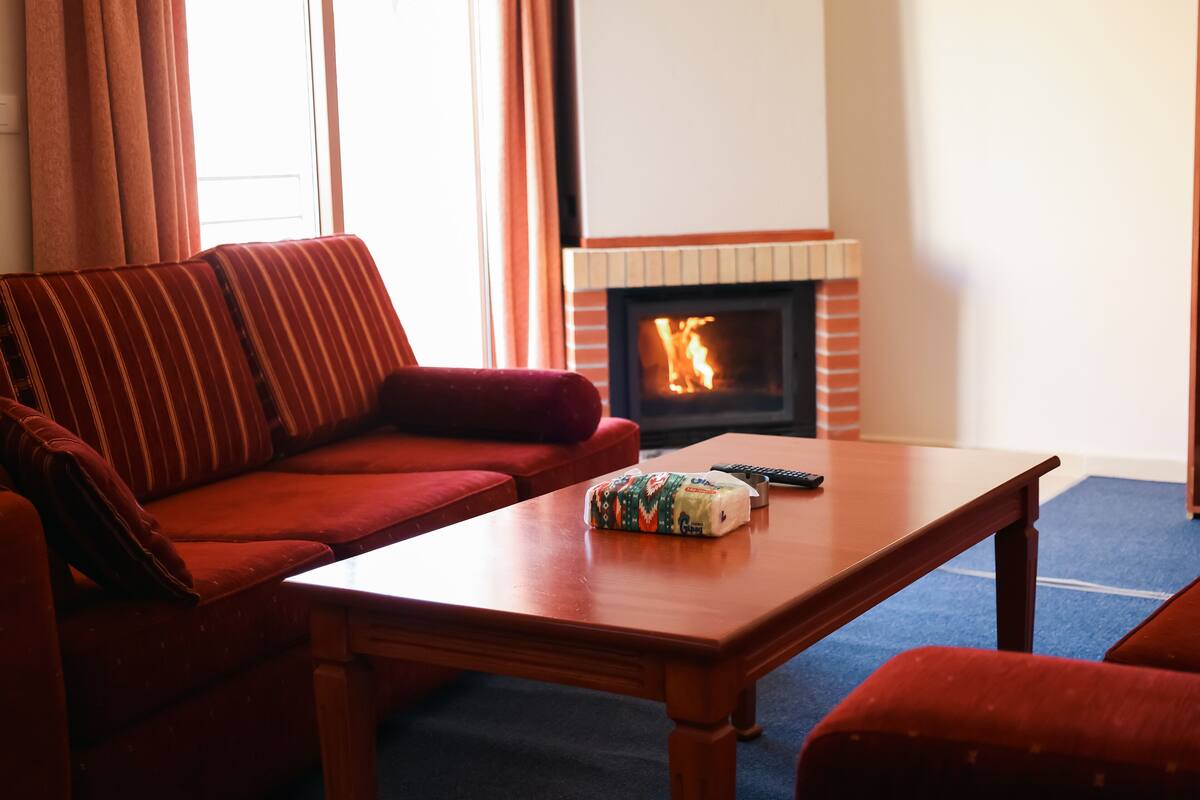 A living room with a red sofa, a wooden coffee table, and a fireplace.