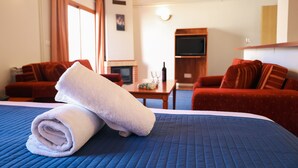 Habitación de hotel con una cama, dos sofás rojos, una televisión y una mesita con una botella y vasos.