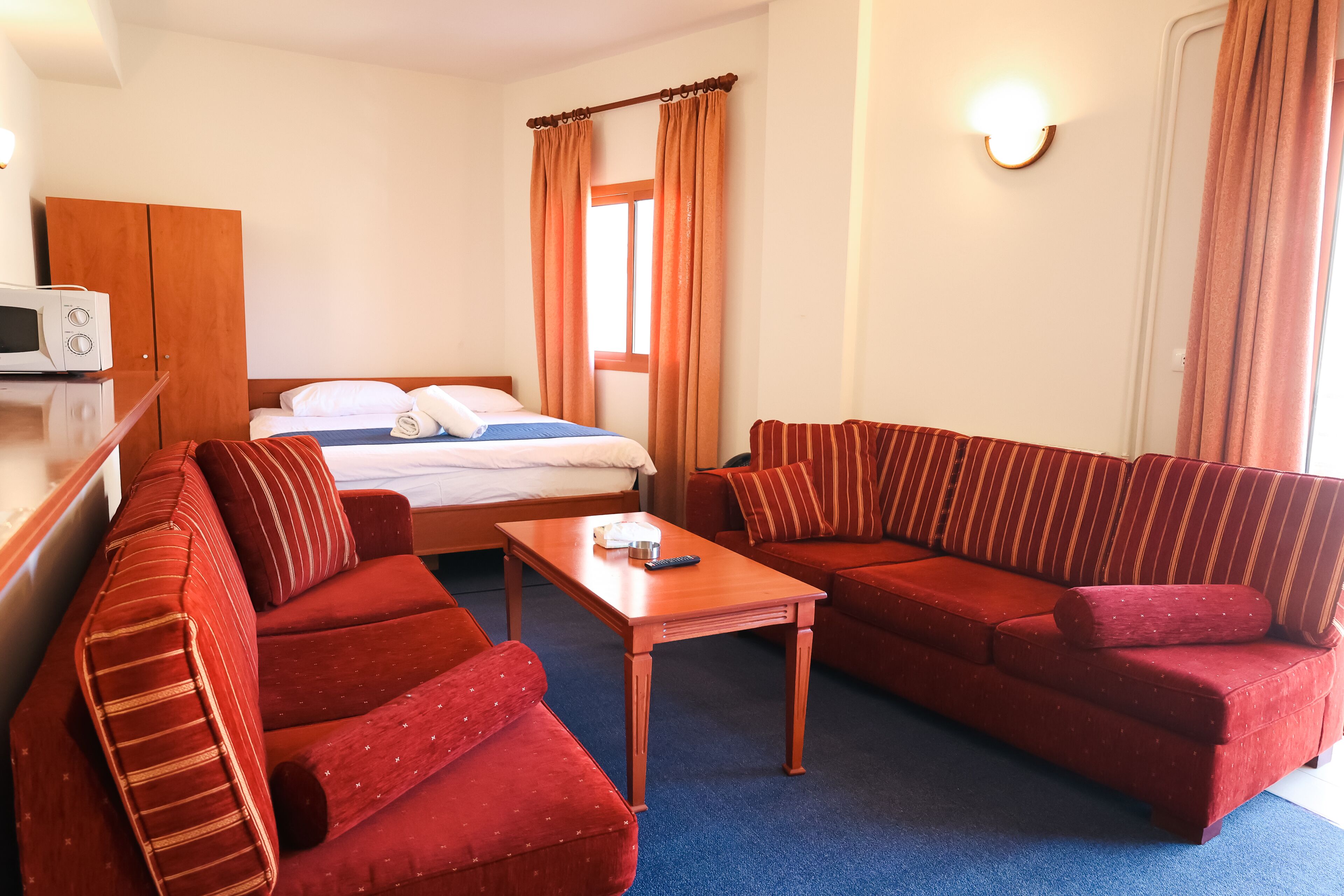 A hotel room with a bed, two red sofas, a wooden coffee table, a microwave, and a wardrobe.