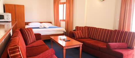 A hotel room with a bed, two red sofas, a wooden coffee table, a microwave, and a wardrobe.
