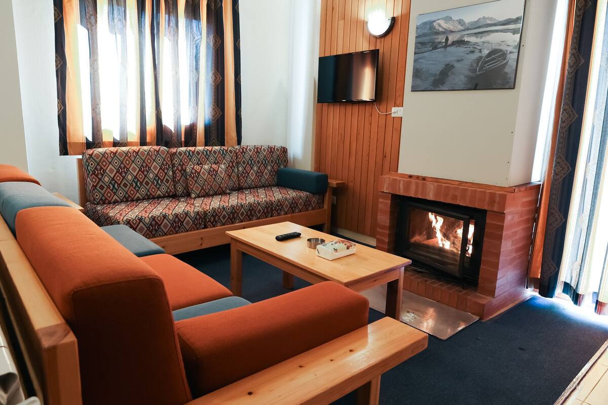 A living room with a sofa, a bench, a coffee table, a fireplace, and a television mounted on the wall.