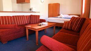 Habitación de hotel con sofá rojo, una mesa de madera, cama con ropa blanca y un armario de madera.
