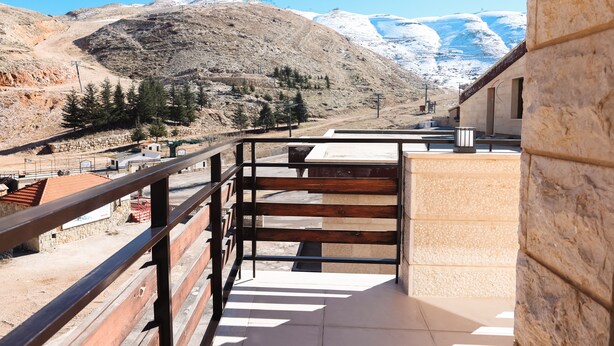 Un balcón con vista a un paisaje montañoso, un muro de piedra y una reja de metal.