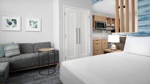 A modern hotel room with a bed, a sofa, a small table, a wardrobe, and a kitchenette. - TownePlace Suites Jacksonville Airport (Jacksonville)