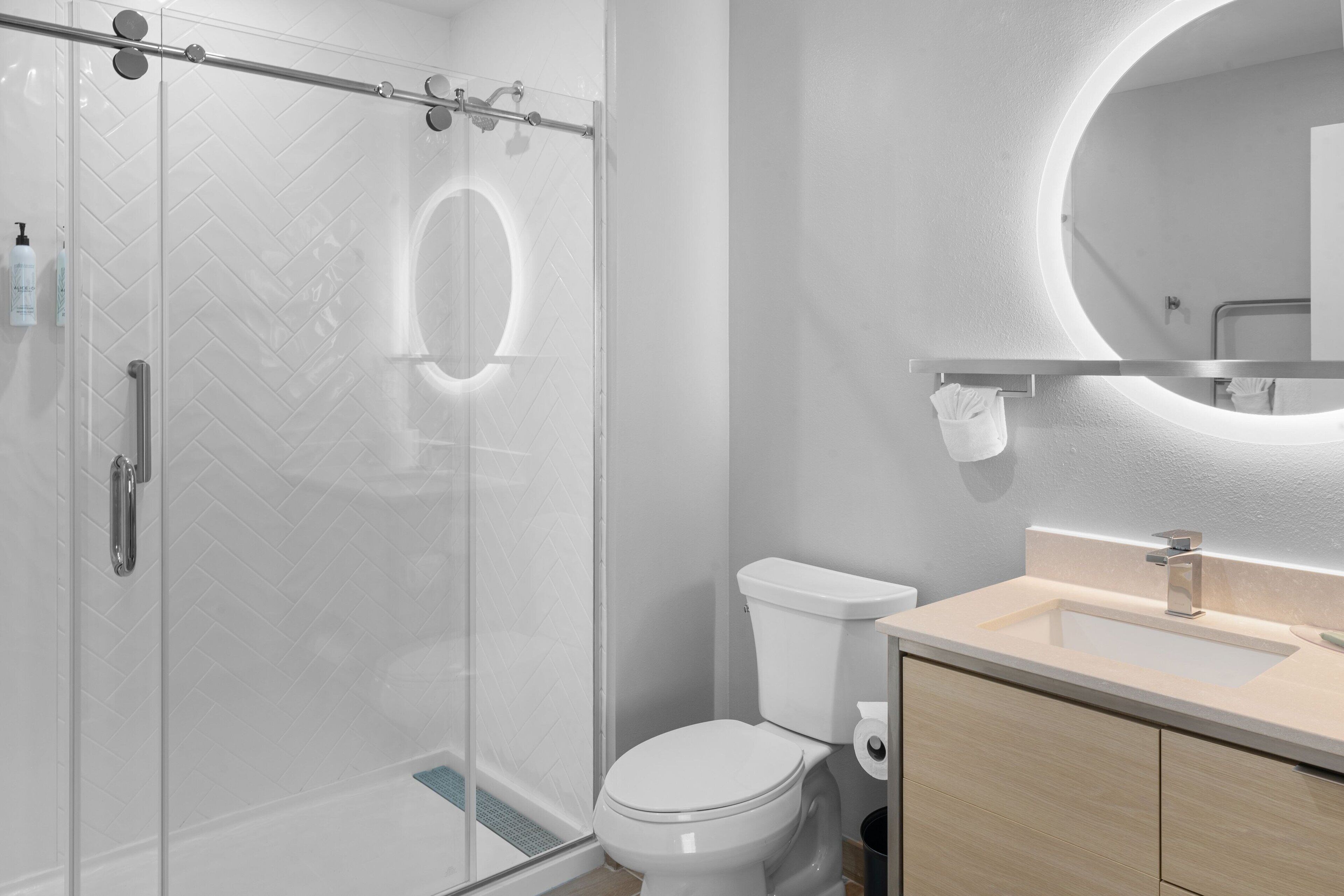 A modern bathroom with a glass shower enclosure, a toilet, and a sink with a mirror above it.