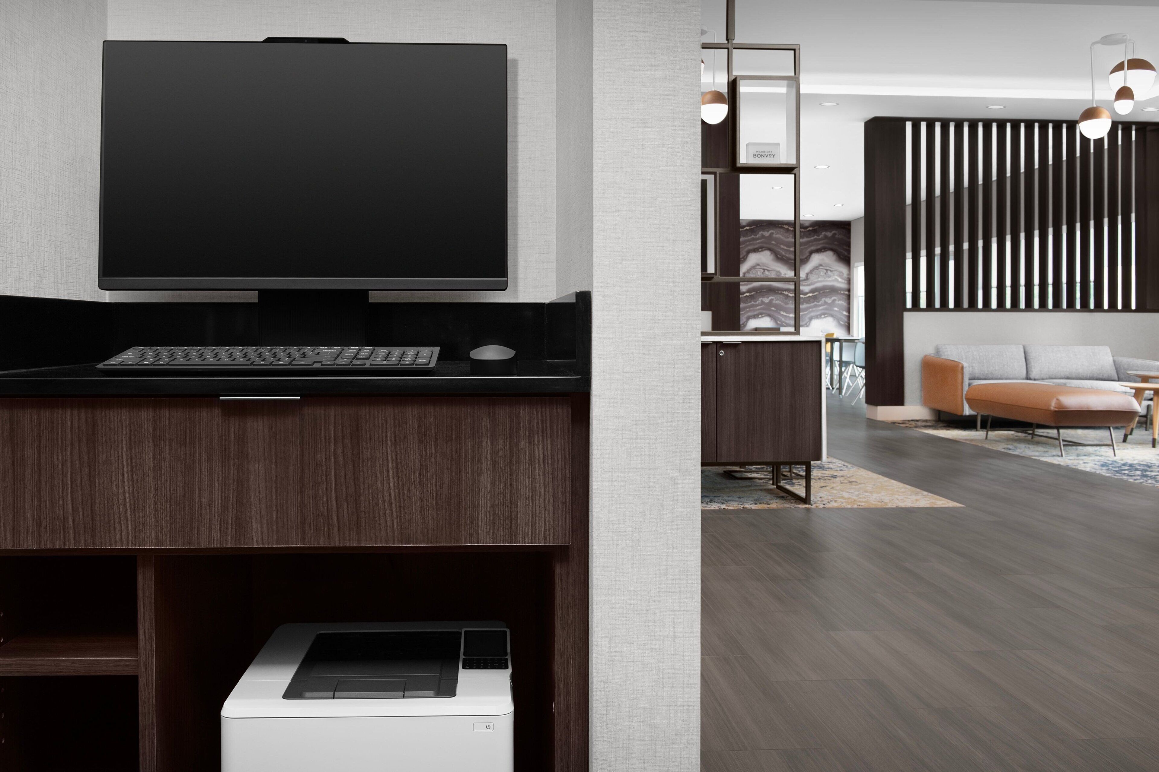 A modern living room with a flat-screen TV, a desktop computer, and a printer on a wooden desk.