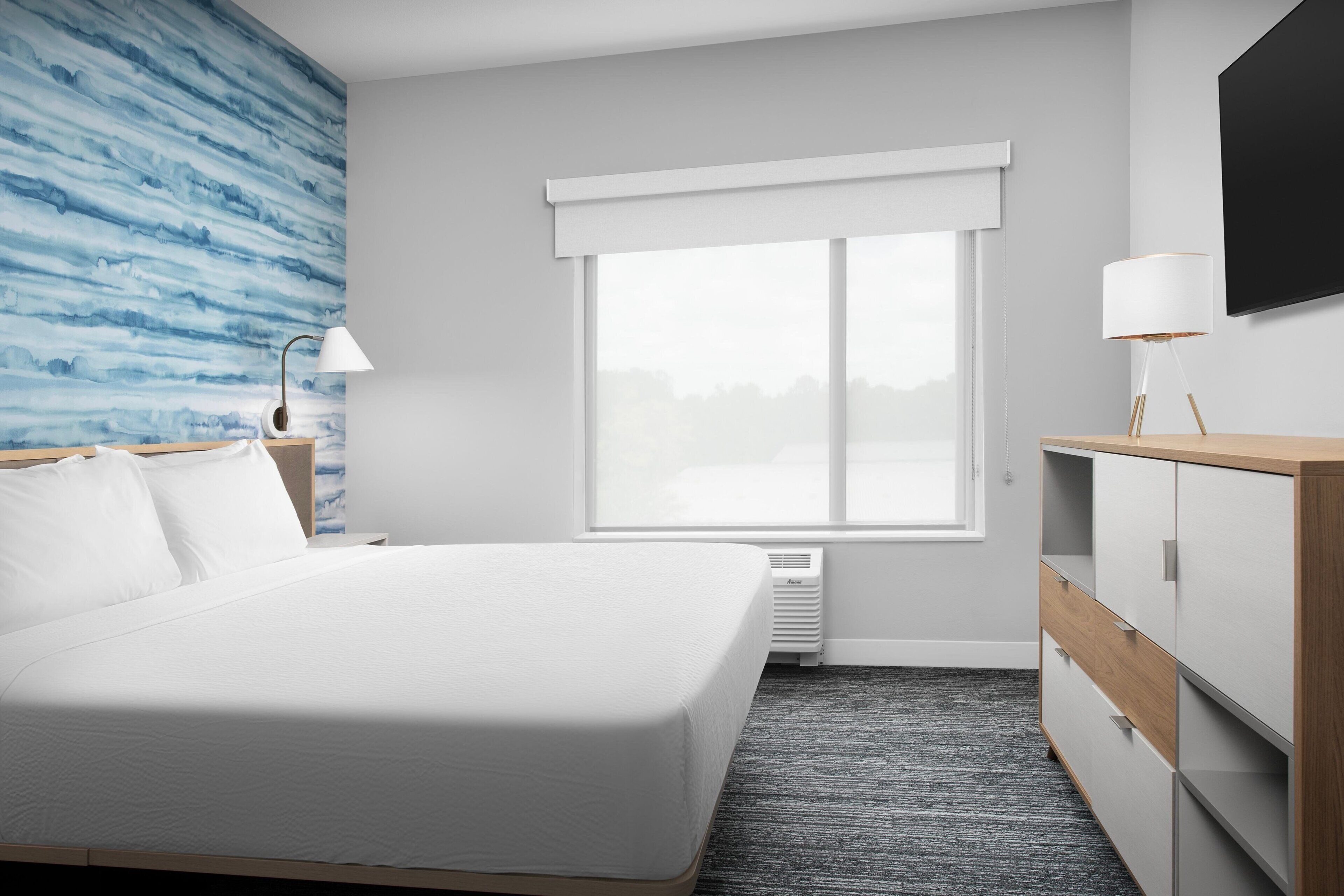 A hotel room with a bed, a dresser, a TV, and a window with blinds.