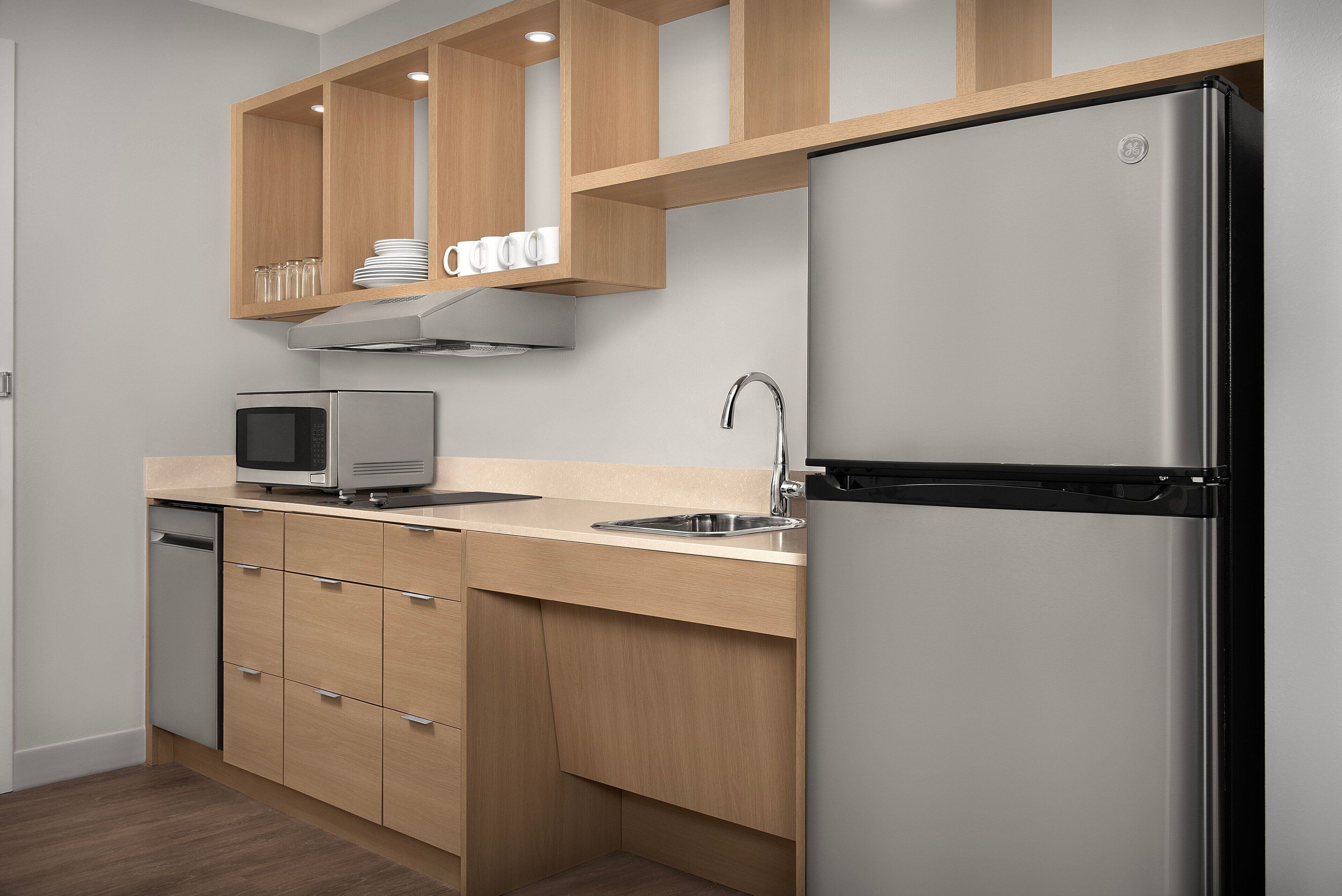 A modern kitchen with wooden cabinets, a stainless steel refrigerator, a microwave, and a dishwasher.