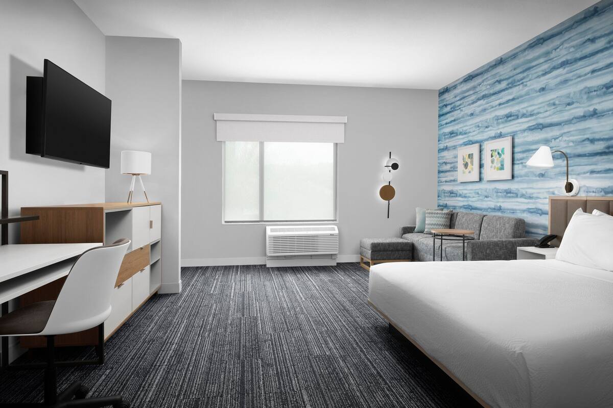 Une chambre d’hôtel moderne équipée d’une télévision à écran plat, d’un bureau avec une chaise, d’un lit, d’un canapé et d’une petite table.
