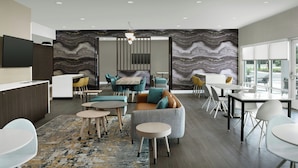 A modern interior with a sofa, chairs, a dining table, and a TV mounted on the wall. - TownePlace Suites Jacksonville Airport (Jacksonville)