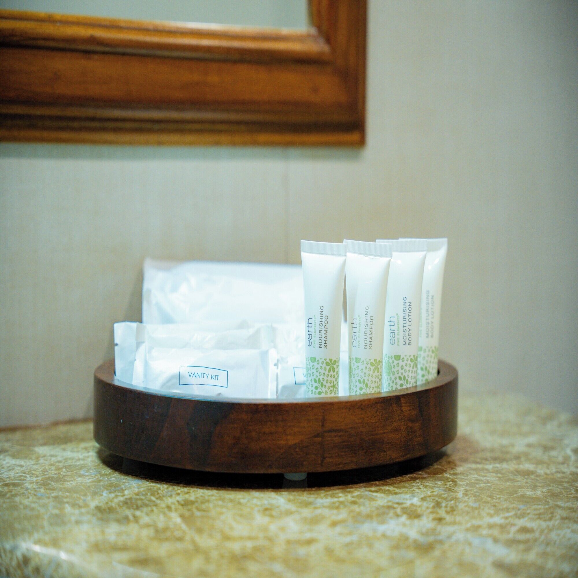 A wooden tray with toiletries on a marble countertop.