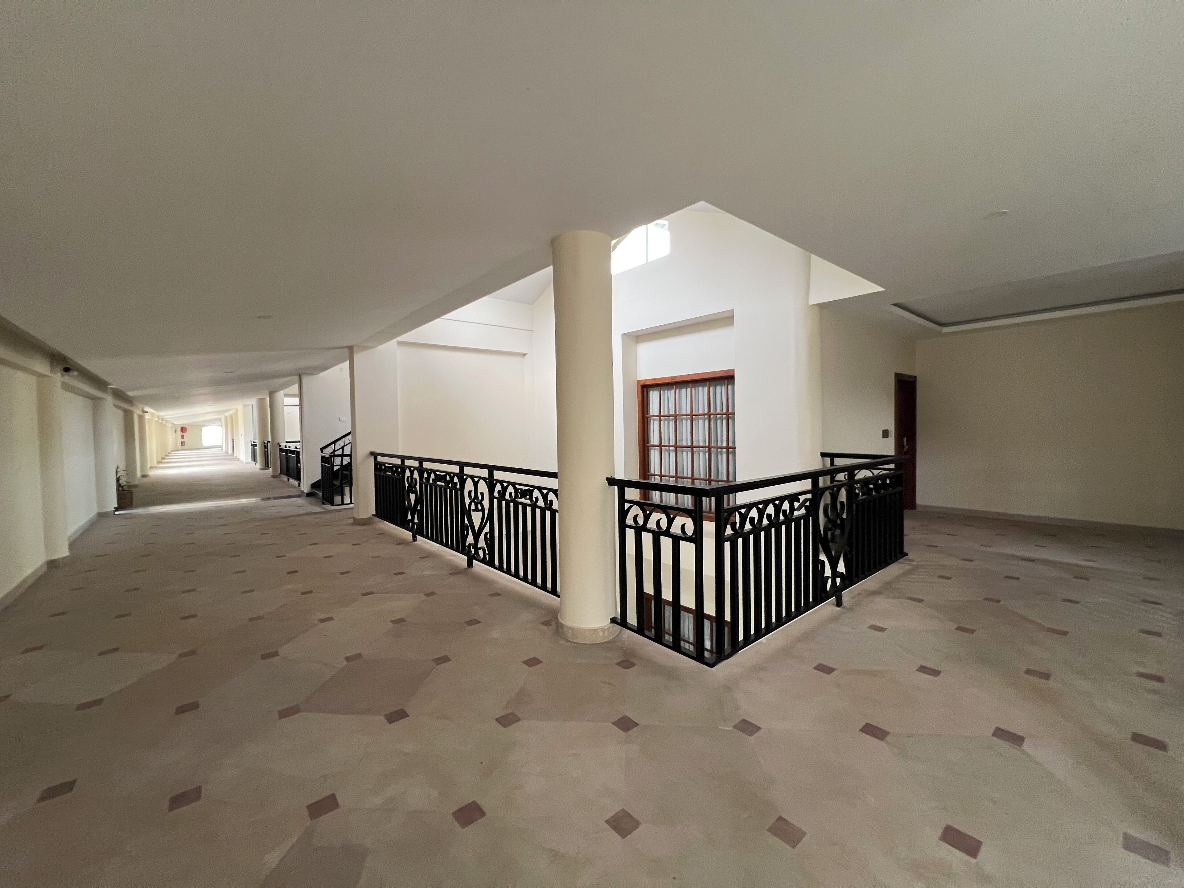 A spacious corridor with patterned flooring, a central column, and a black railing.