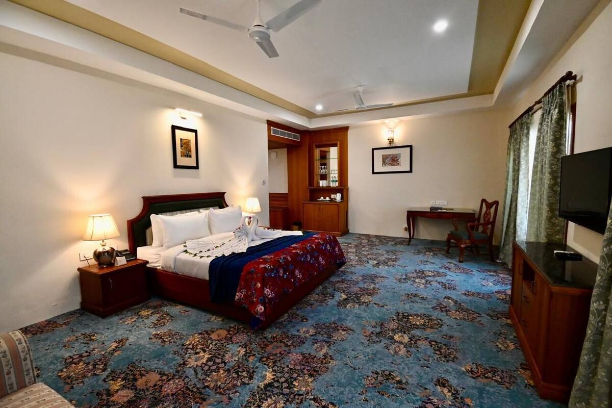 A hotel room with a bed, nightstands, a desk, a television, and a ceiling fan.