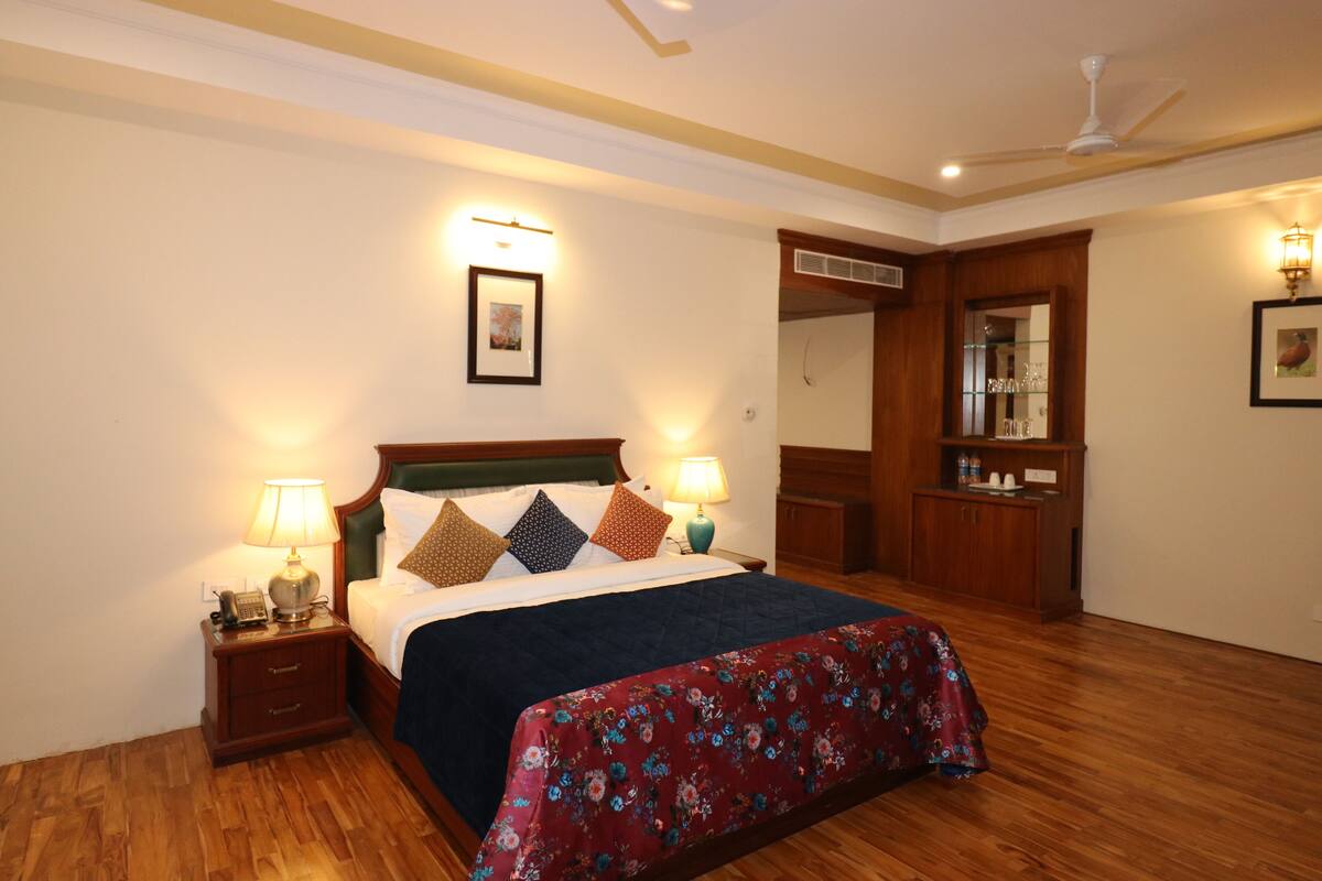 A bedroom with a large bed, two bedside tables with lamps, a wooden headboard, a red floral bedspread, and a wooden wardrobe.