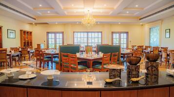 A spacious dining area with multiple tables and chairs, a central chandelier, and large windows allowing natural light.