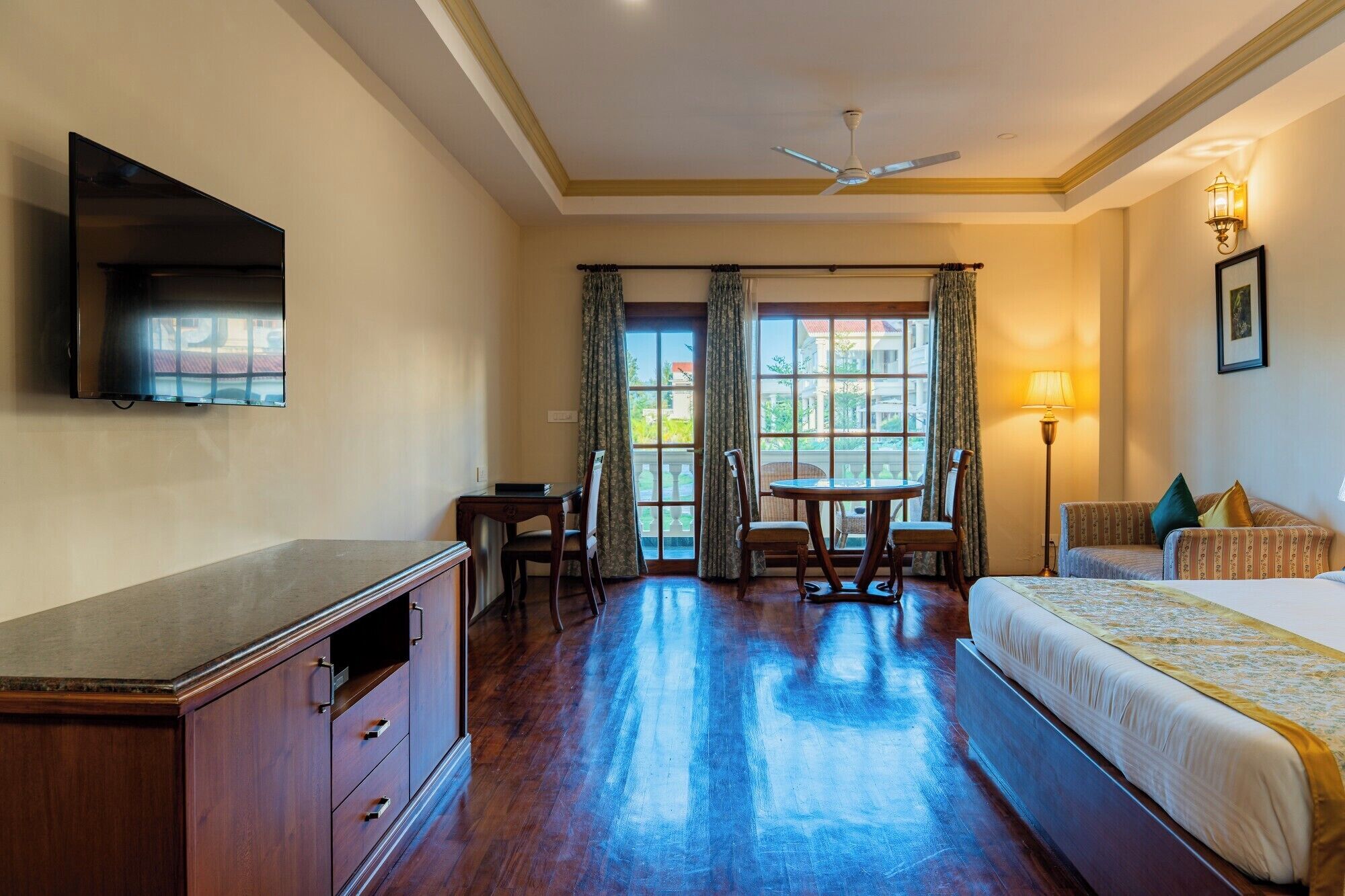 A hotel room with a bed, a desk, a chair, a television, a ceiling fan, and a window with curtains.