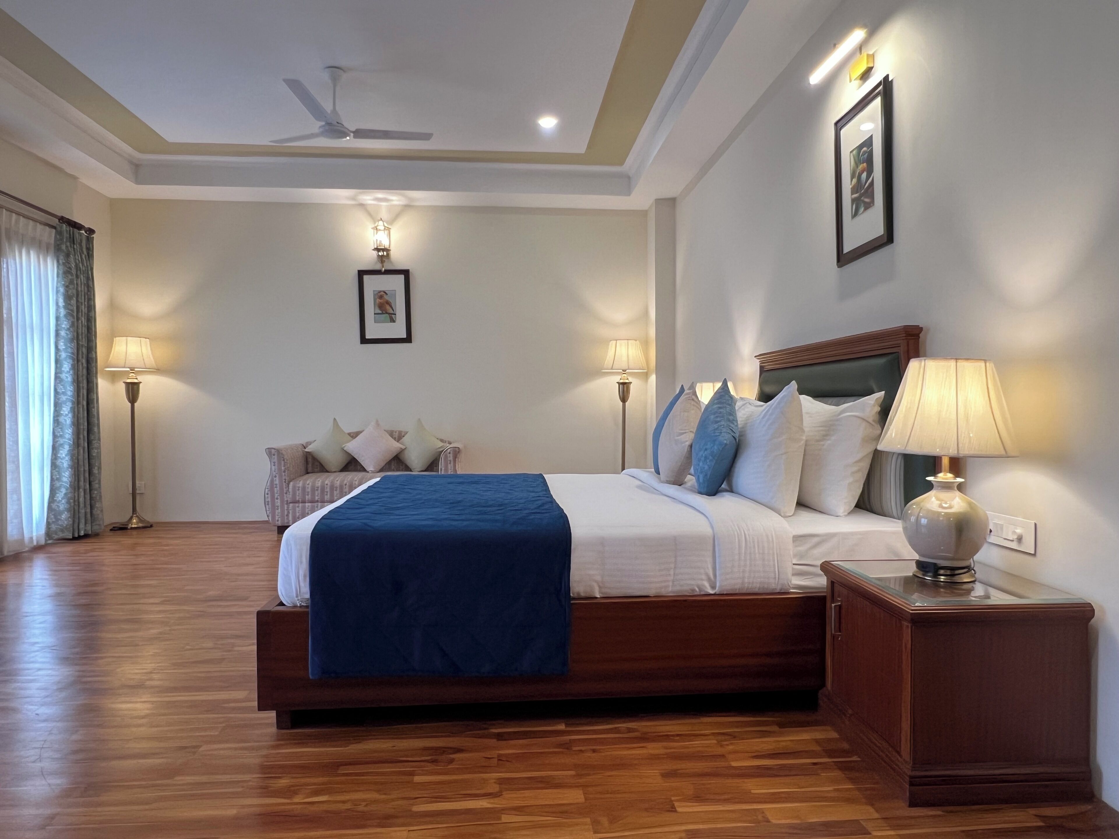 A hotel room with a large bed, two bedside tables, a ceiling fan, and a view of the outdoors.