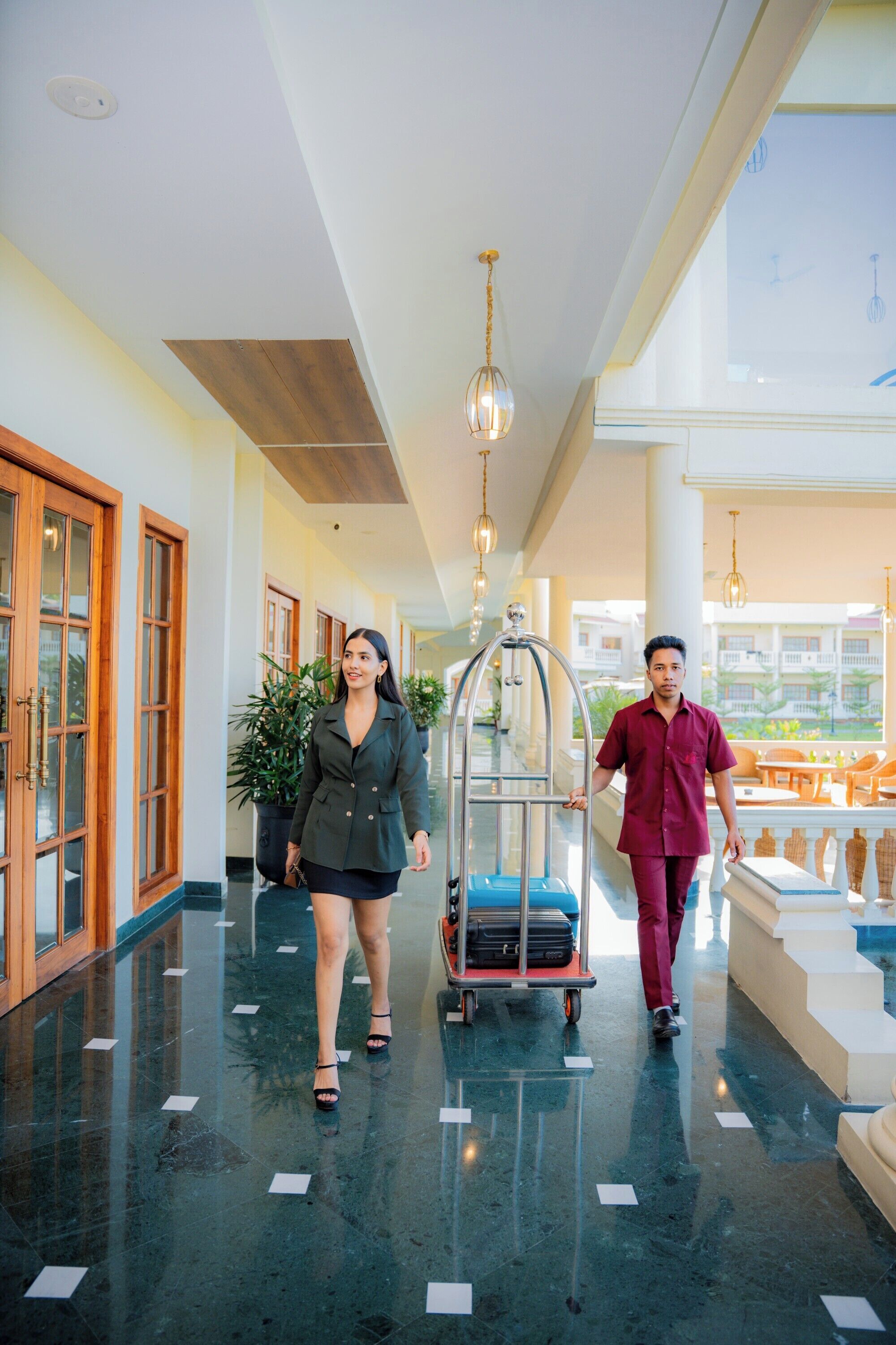 A hotel lobby with a polished floor, wooden doors, and a seating area with tables and chairs.