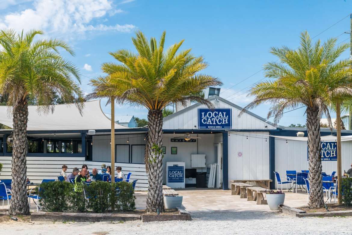Un ristorante chiamato 'Local Catch' con posti a sedere all'aperto e palme.