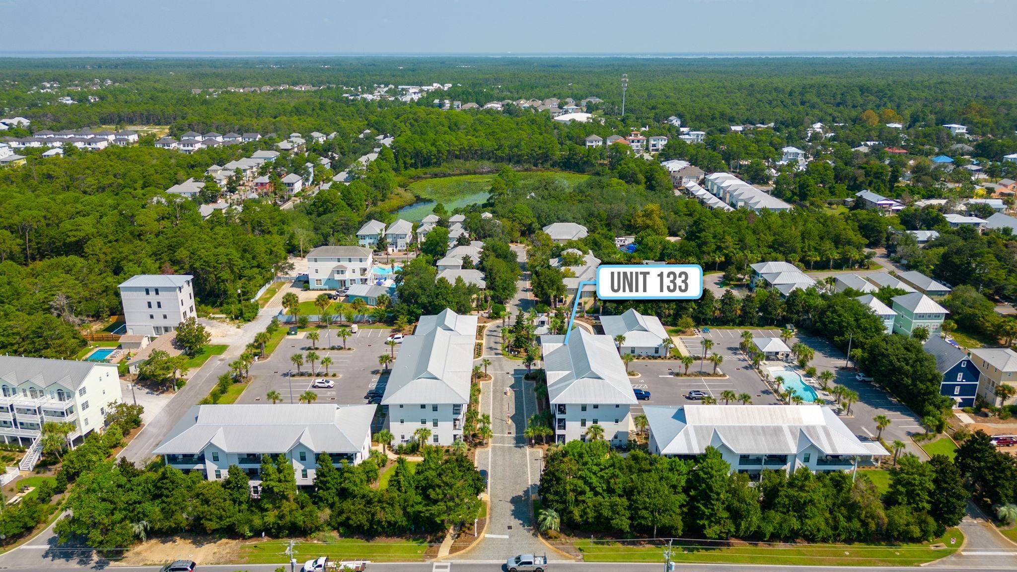 An aerial view of a residential area with multiple houses, a clear road, and a sign indicating "UNIT 133".