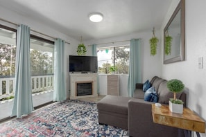 Un salon comprenant un canapé, un téléviseur, une cheminée et un balcon avec des rideaux.