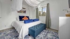 Una camera da letto con un letto, una panca, una finestra con tende e un quadro appeso al muro.